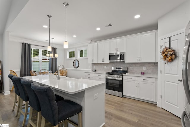 kitchen featuring white cabinets, a kitchen island with sink, appliances with stainless steel finishes, and hanging light fixtures