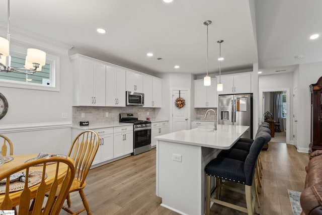 kitchen with pendant lighting, stainless steel appliances, white cabinets, and light hardwood / wood-style floors