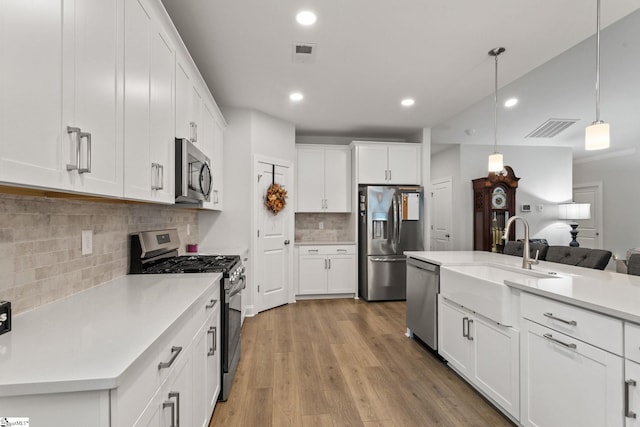 kitchen featuring light hardwood / wood-style floors, tasteful backsplash, white cabinets, hanging light fixtures, and appliances with stainless steel finishes