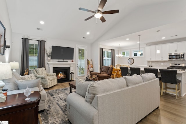 living room featuring light wood-type flooring, ceiling fan with notable chandelier, lofted ceiling, and sink