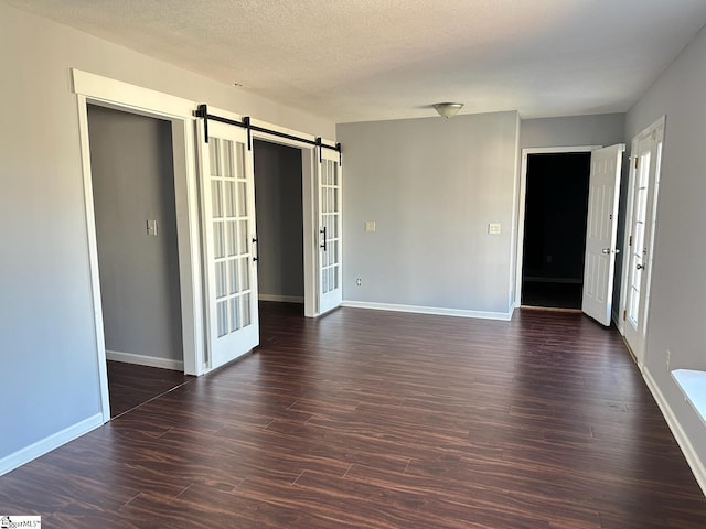 empty room with a barn door, french doors, and dark wood-type flooring