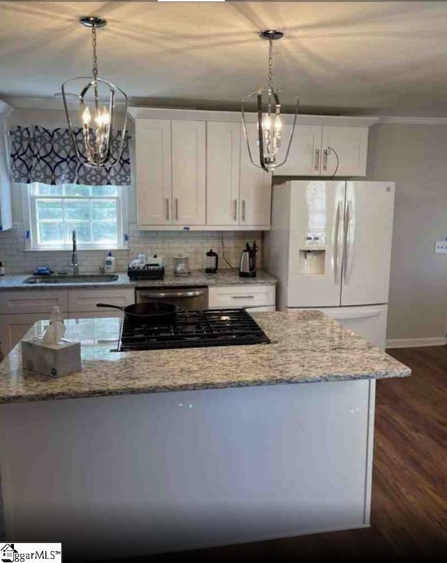 kitchen featuring white cabinetry, white fridge with ice dispenser, sink, hanging light fixtures, and light stone counters