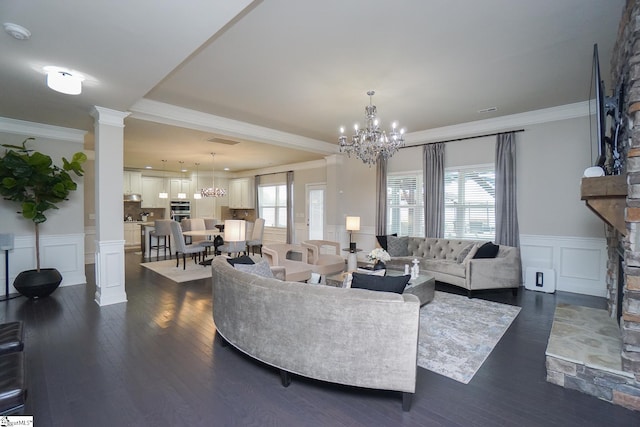 living room featuring dark wood-type flooring, a fireplace, crown molding, an inviting chandelier, and decorative columns