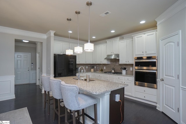 kitchen featuring white cabinetry, stainless steel appliances, decorative light fixtures, a center island with sink, and sink