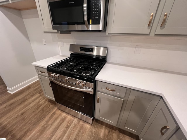 kitchen with gray cabinetry, stainless steel appliances, light countertops, backsplash, and dark wood-style floors