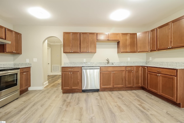 kitchen featuring appliances with stainless steel finishes, light stone countertops, light hardwood / wood-style flooring, and sink