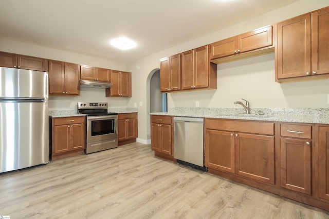 kitchen with light stone countertops, stainless steel appliances, light hardwood / wood-style floors, and sink