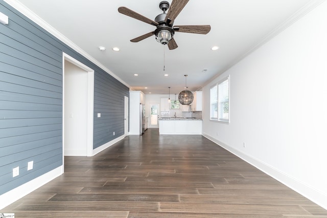 unfurnished living room featuring crown molding, wood walls, dark hardwood / wood-style floors, and ceiling fan