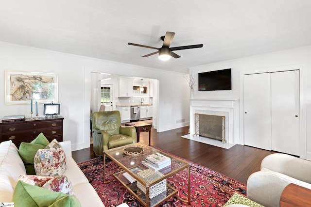 living room with ceiling fan, sink, a fireplace, crown molding, and dark hardwood / wood-style flooring