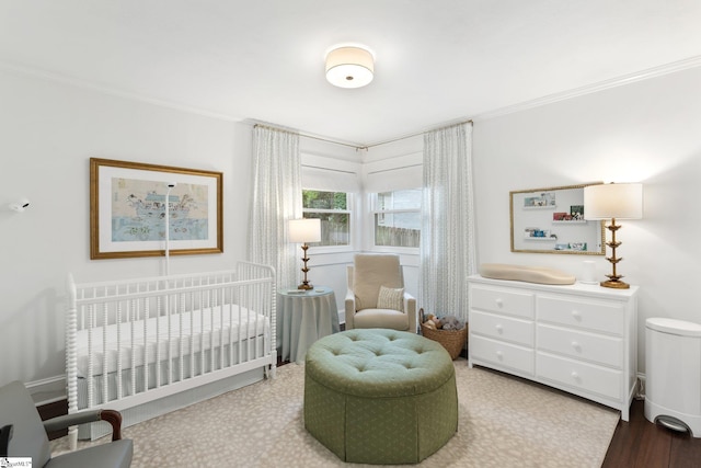 bedroom with a crib, ornamental molding, and hardwood / wood-style flooring