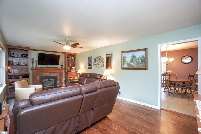 living room with dark hardwood / wood-style flooring, a brick fireplace, and ceiling fan with notable chandelier