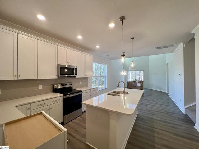 kitchen with appliances with stainless steel finishes, decorative light fixtures, white cabinetry, sink, and a center island with sink