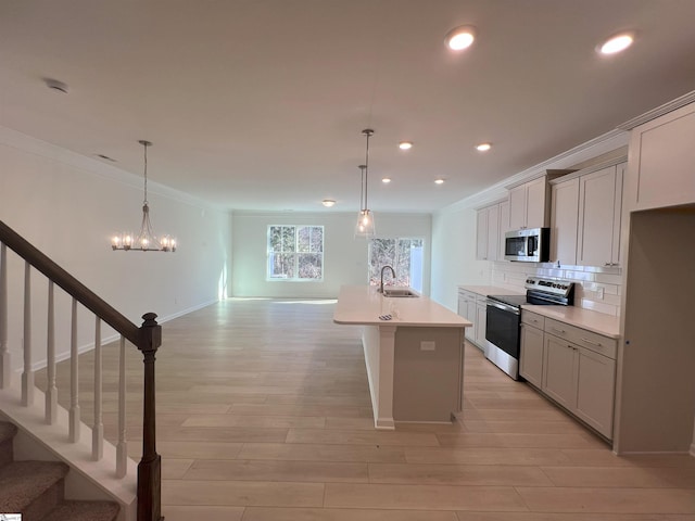 kitchen featuring appliances with stainless steel finishes, pendant lighting, tasteful backsplash, sink, and a center island with sink