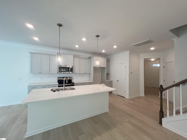 kitchen with decorative light fixtures, light hardwood / wood-style floors, sink, appliances with stainless steel finishes, and an island with sink