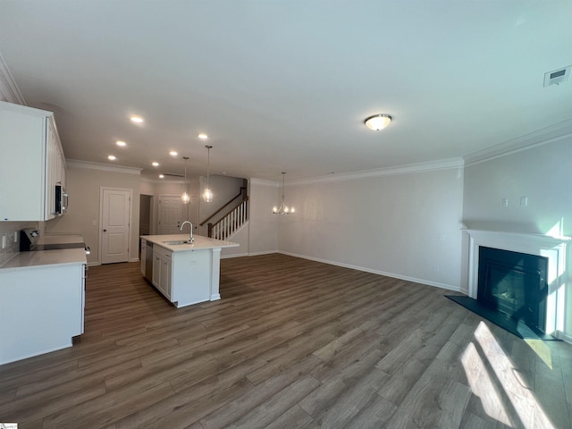 kitchen featuring white cabinets, an island with sink, sink, hanging light fixtures, and ornamental molding