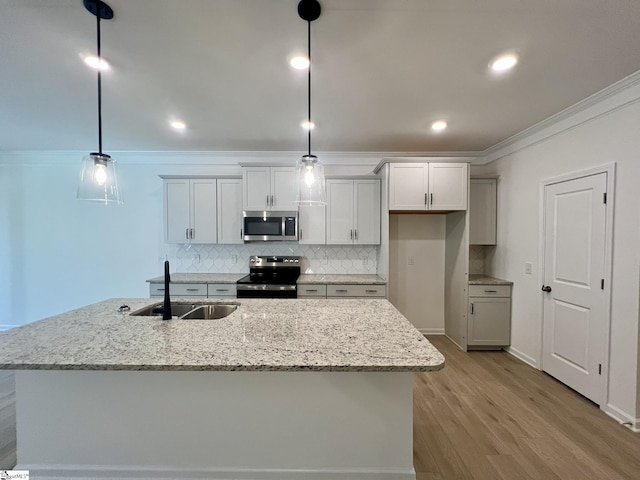 kitchen with an island with sink, appliances with stainless steel finishes, decorative light fixtures, light stone counters, and sink