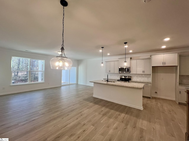 kitchen featuring a center island with sink, light stone countertops, appliances with stainless steel finishes, and pendant lighting