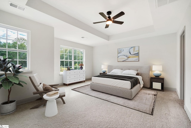 carpeted bedroom with ceiling fan, a tray ceiling, and multiple windows