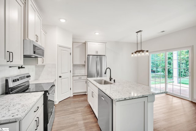 kitchen featuring pendant lighting, stainless steel appliances, white cabinetry, and a kitchen island with sink