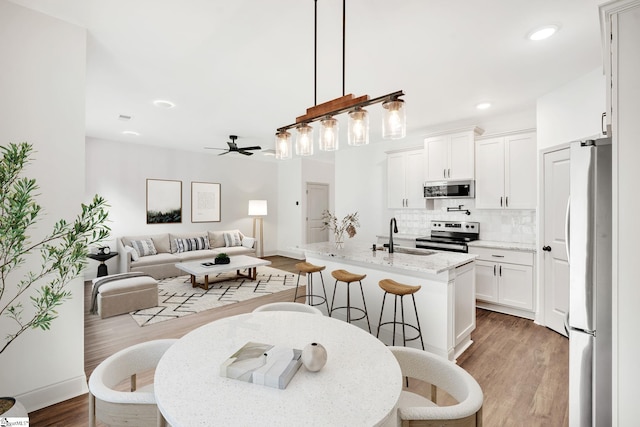 interior space featuring ceiling fan, white cabinets, pendant lighting, stainless steel appliances, and light hardwood / wood-style floors