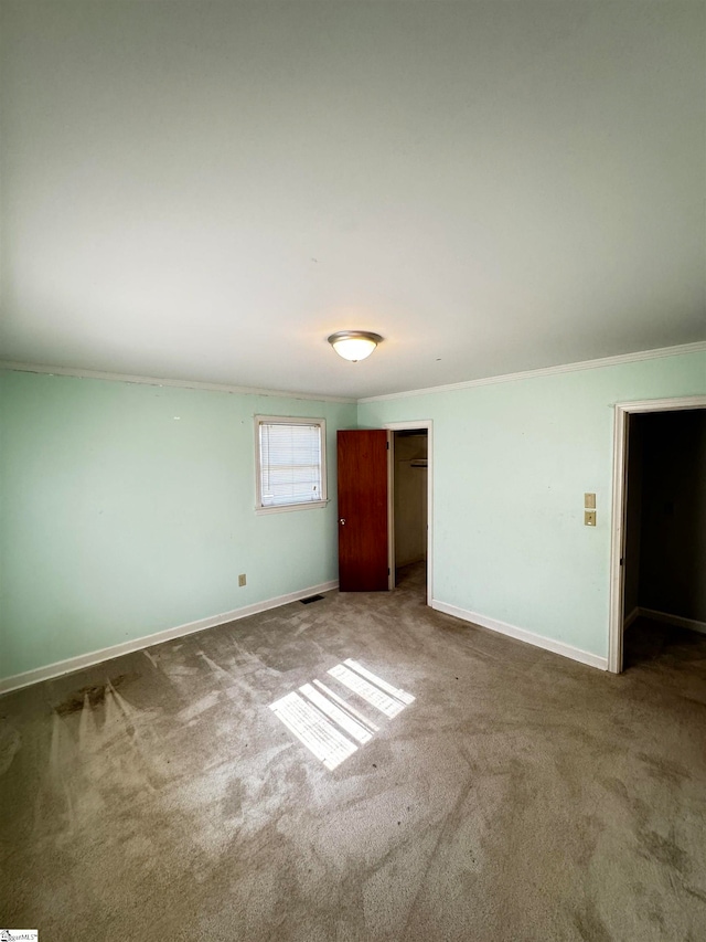 unfurnished bedroom featuring a closet, ornamental molding, a spacious closet, and carpet