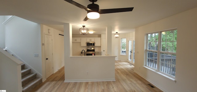 kitchen with white cabinets, light wood-type flooring, tasteful backsplash, stainless steel appliances, and ceiling fan with notable chandelier