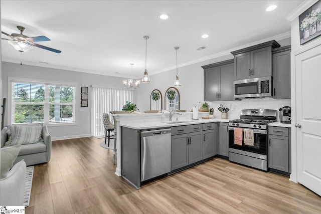 kitchen featuring light hardwood / wood-style floors, ceiling fan with notable chandelier, kitchen peninsula, hanging light fixtures, and stainless steel appliances