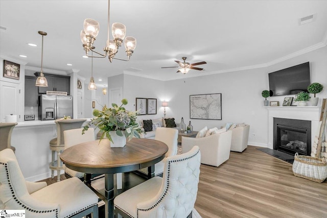 dining space featuring light wood-type flooring, ceiling fan with notable chandelier, and ornamental molding