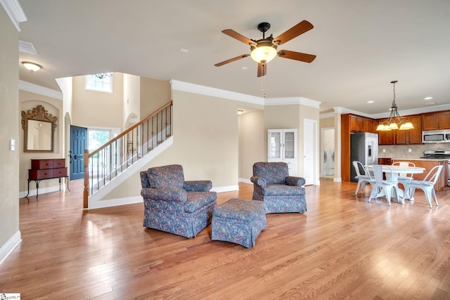 living room featuring washer / dryer, ceiling fan with notable chandelier, light wood-type flooring, and crown molding