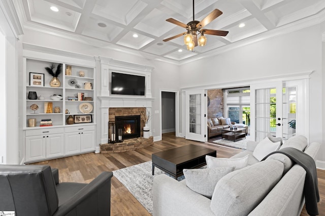 living room featuring ceiling fan, beam ceiling, light hardwood / wood-style flooring, coffered ceiling, and a fireplace