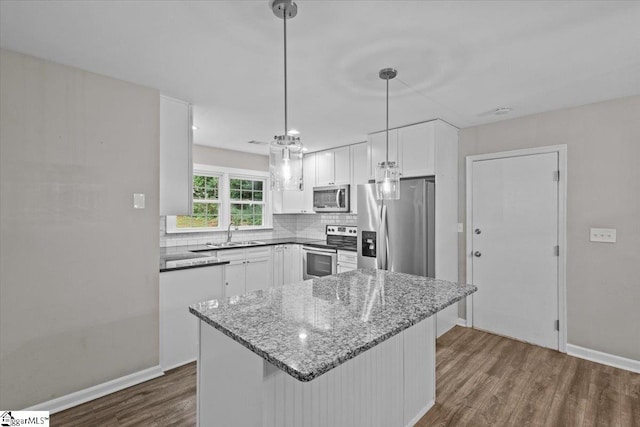 kitchen with pendant lighting, white cabinetry, stainless steel appliances, dark stone counters, and dark hardwood / wood-style flooring