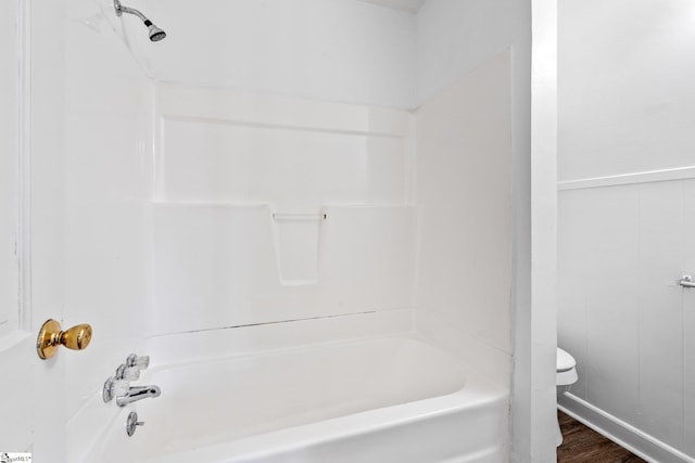 full bath with toilet, shower / tub combination, wood finished floors, and wainscoting