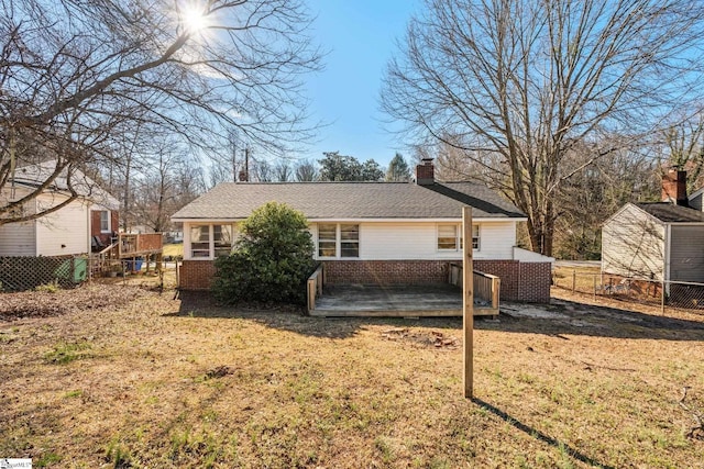 back of house with brick siding, a yard, a chimney, fence, and a deck