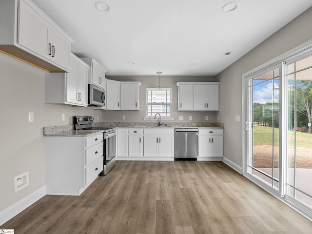 kitchen with appliances with stainless steel finishes, white cabinetry, pendant lighting, light wood-type flooring, and sink