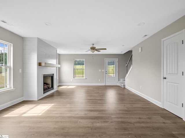 unfurnished living room with wood-type flooring, ceiling fan, a large fireplace, and a healthy amount of sunlight