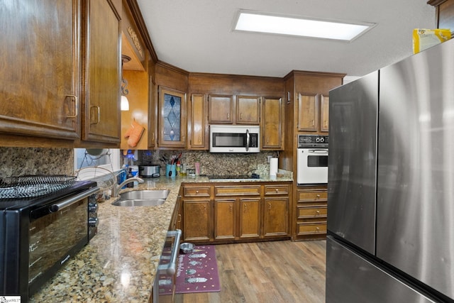 kitchen with appliances with stainless steel finishes, tasteful backsplash, light stone countertops, light hardwood / wood-style flooring, and sink