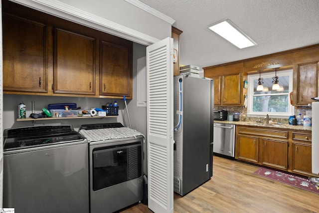 kitchen featuring light wood-type flooring, sink, appliances with stainless steel finishes, decorative light fixtures, and washing machine and dryer