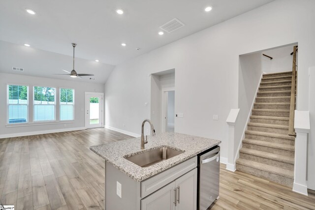 kitchen featuring dishwasher, lofted ceiling, sink, a kitchen island with sink, and light stone countertops