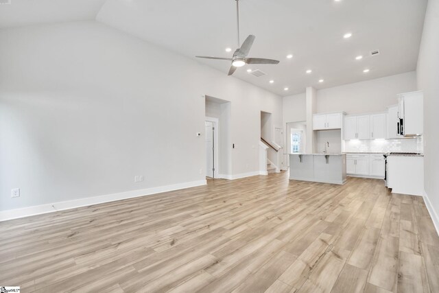 unfurnished living room featuring ceiling fan, sink, high vaulted ceiling, and light hardwood / wood-style floors