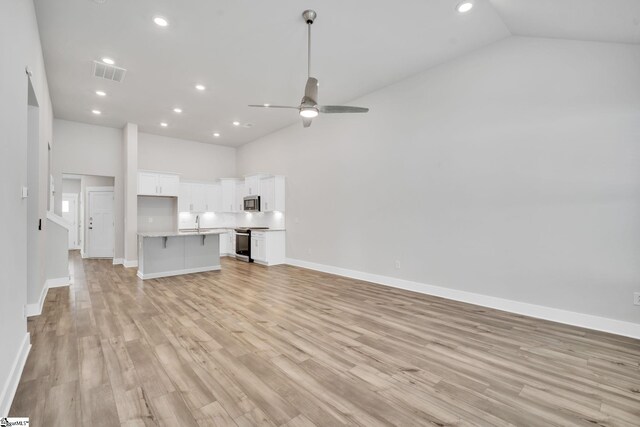 unfurnished living room with ceiling fan, light wood-type flooring, sink, and high vaulted ceiling