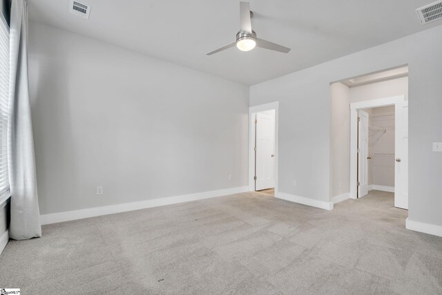 unfurnished bedroom with a spacious closet, light colored carpet, ceiling fan, and a closet