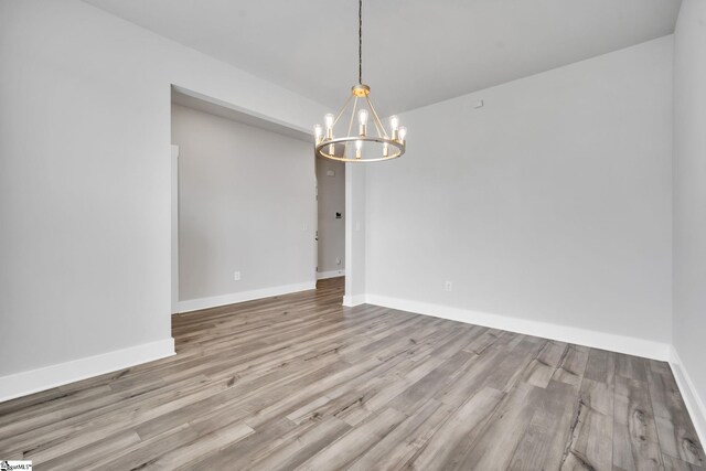 unfurnished room featuring a chandelier and light wood-type flooring