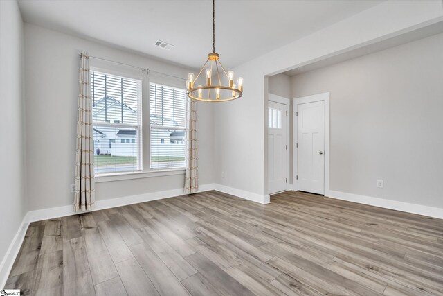 spare room with a notable chandelier, hardwood / wood-style floors, and a wealth of natural light