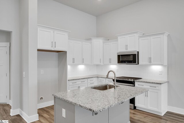 kitchen with sink, appliances with stainless steel finishes, white cabinetry, light stone counters, and a center island with sink