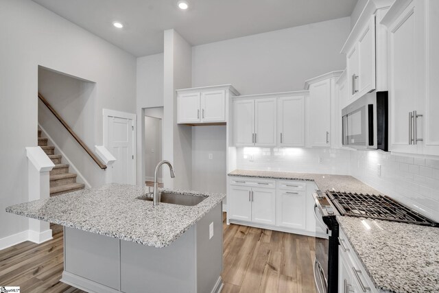 kitchen with white cabinetry, stainless steel appliances, light stone countertops, and sink