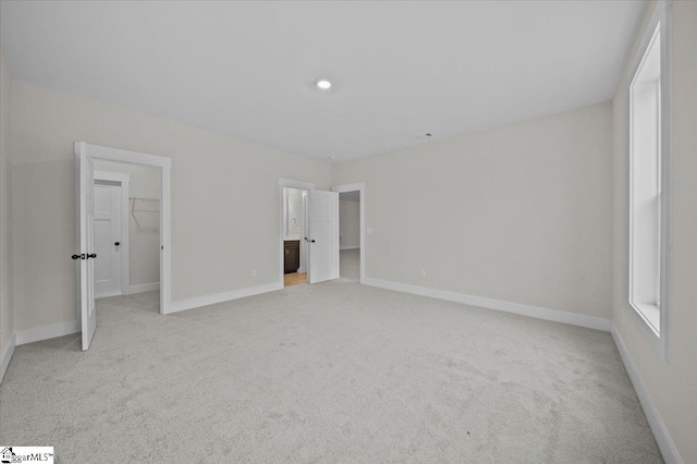 unfurnished bedroom with ensuite bath, a walk in closet, light colored carpet, and a closet