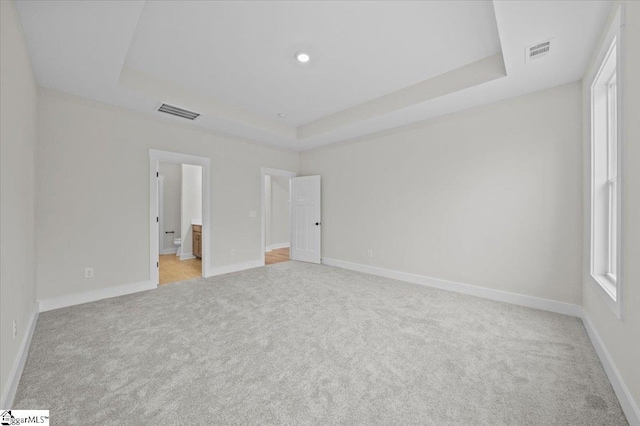 unfurnished bedroom featuring light carpet, connected bathroom, a tray ceiling, and multiple windows