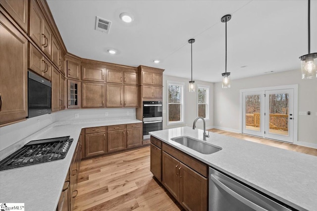 kitchen featuring light wood-type flooring, decorative light fixtures, sink, and black appliances