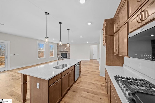 kitchen with sink, a center island with sink, light hardwood / wood-style flooring, pendant lighting, and stainless steel appliances