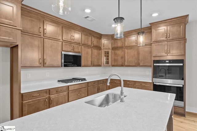 kitchen featuring sink, light hardwood / wood-style floors, hanging light fixtures, and appliances with stainless steel finishes